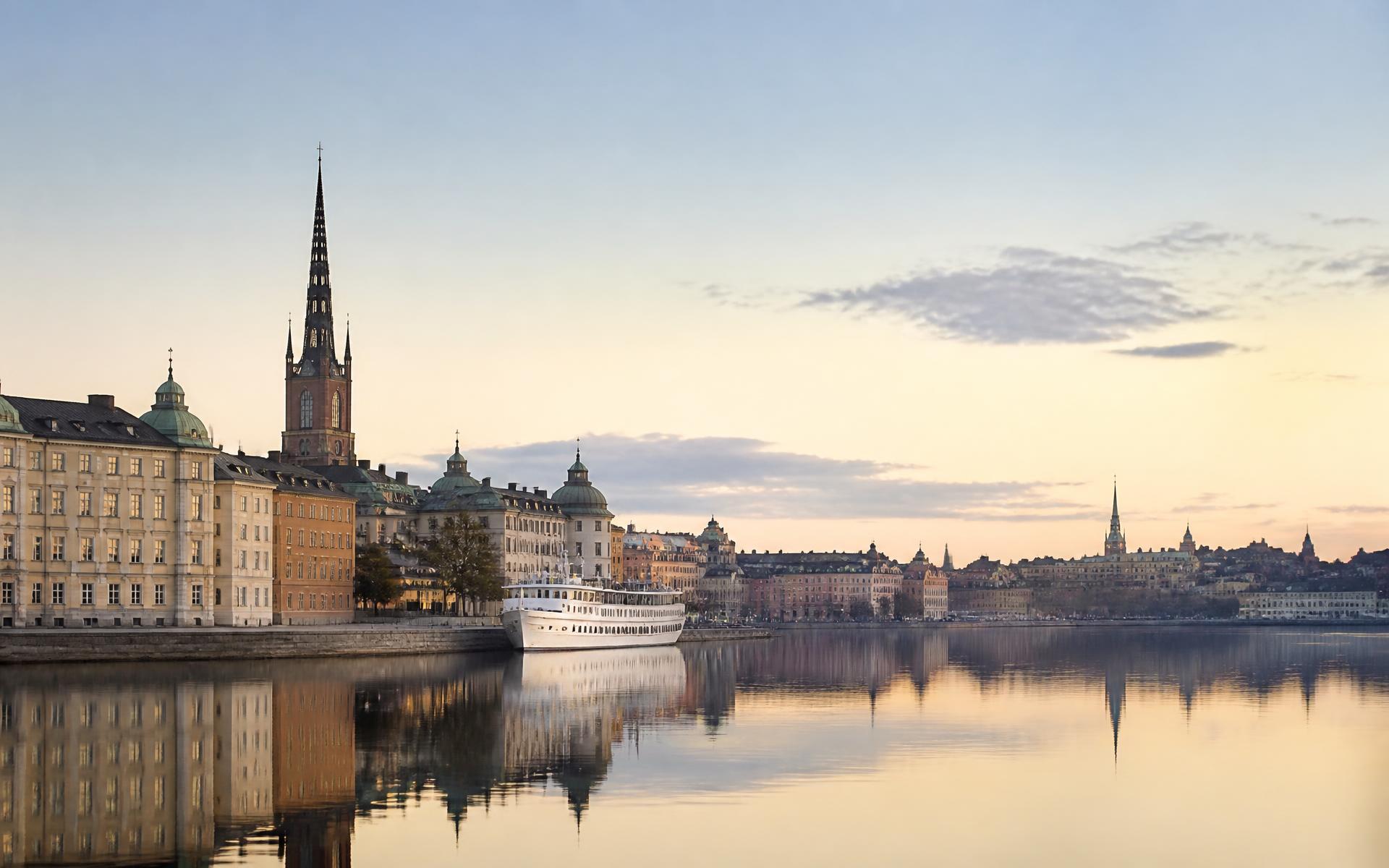 Stockholm waterfront at dawn, with the spires of Gamla Stan reflected in still water under pale Nordic light